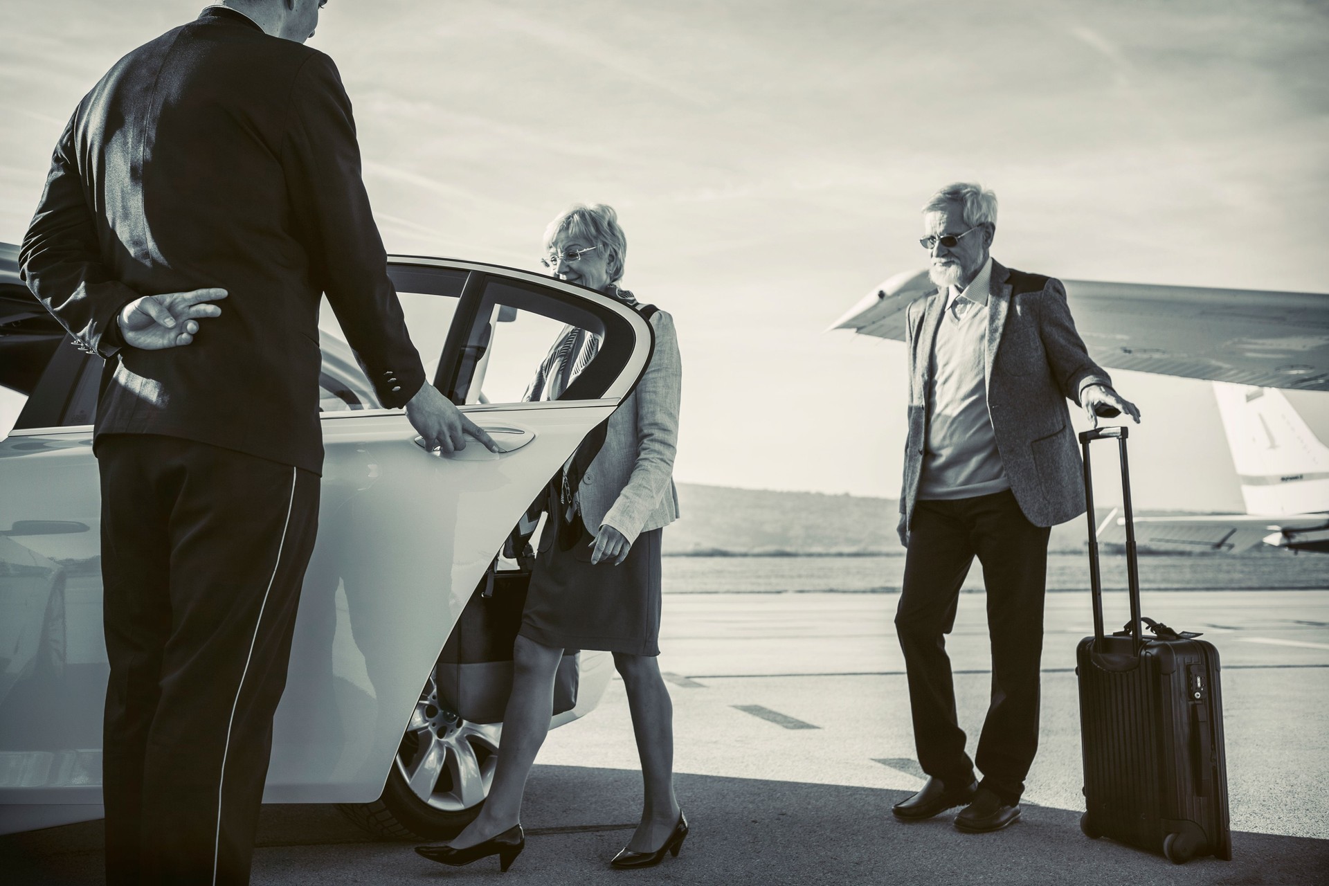 Driver helping senior adult couple into limousine at airport